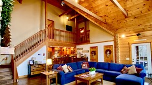 Ein geräumiges Wohnzimmer mit Holzboden, einem blauen Sofagarnitur, einem Holztisch und einer Treppe, die in eine obere Etage führt.