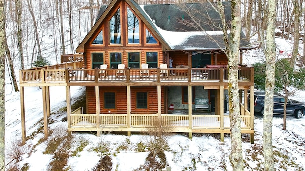 Eine Blockhütte mit Balkon und Terrasse, umgeben von schneebedeckten Bäumen.