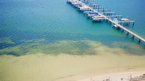 Uma praia com piscina translúcida e um píer que se estende para o oceano.