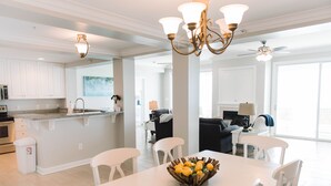 Una cocina moderna con armarios blancos, un comedor con mesa y sillas blancas, y una isla central con un frutero.
