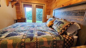 A bedroom with a large bed, a wooden headboard, a nightstand with a lamp, and a sign on the door.