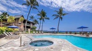 A pool area with lounge chairs, a hot tub, and palm trees.