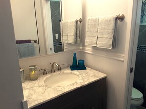 A bathroom with a marble sink, two faucets, a mirror, and two towels hanging on a towel rack. - Maui Tranquility ... Relax, Unwind and Feel Welcomed! (Kihei)