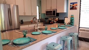 A modern kitchen with stainless steel appliances, a granite countertop, and teal-colored plates and glasses set for dining. - Maui Tranquility ... Relax, Unwind and Feel Welcomed! (Kihei)