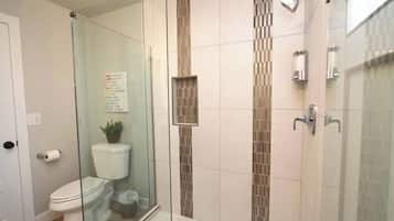A bathroom with a glass shower enclosure, a toilet, and a sink.