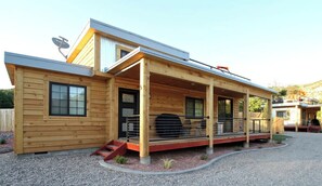 Een moderne houten blokhut met een overdekte veranda, een schotelantenne en een barbecueplaats.