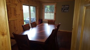 A wooden dining room with a large table and chairs, a window with a view of a fence, and a sign on the wall that says "GO JUMP IN THE LAKE". - Everything new in this beautiful secluded home. Air conditioning. Wifi. Firepit. (Lexington)