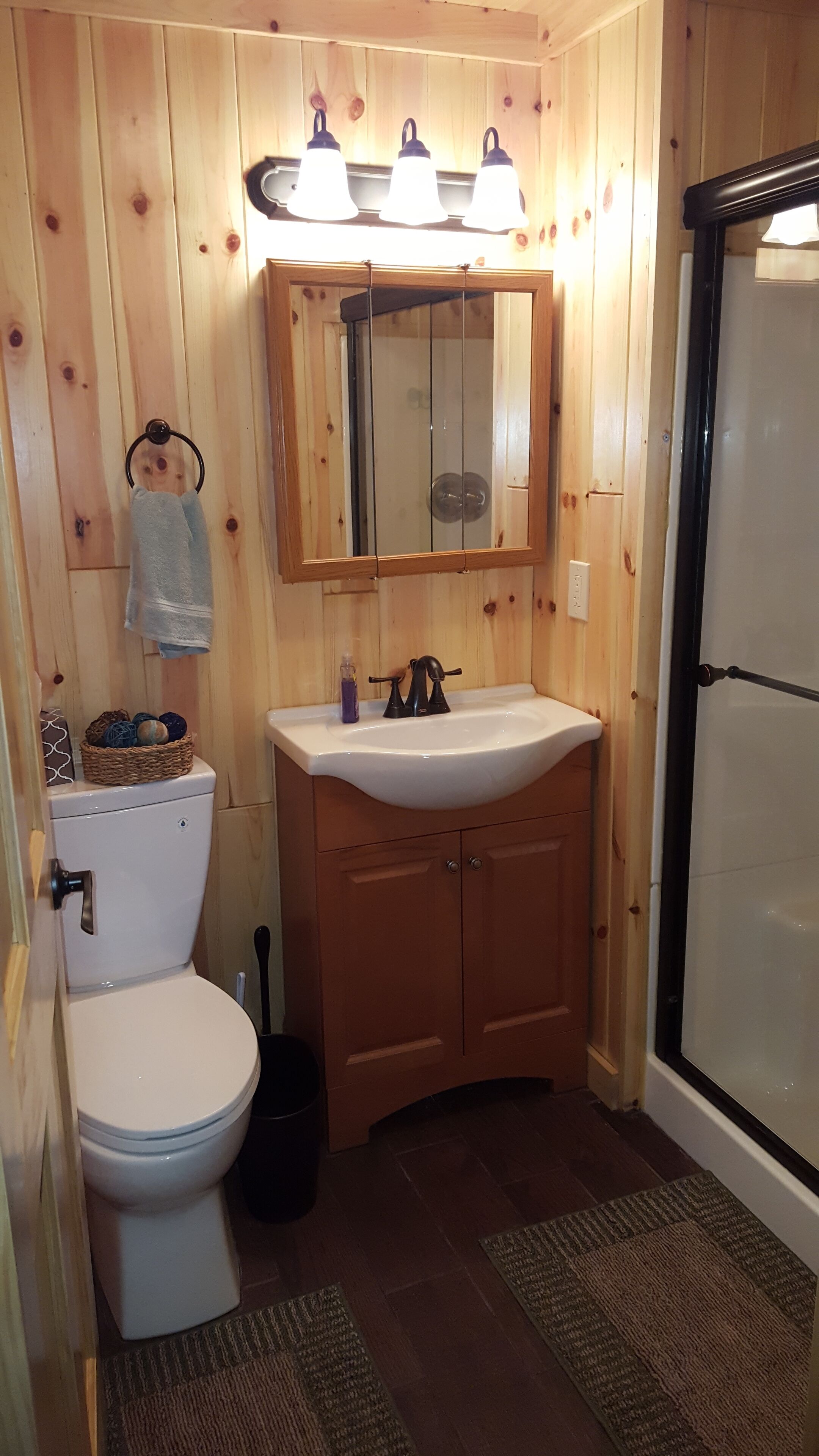 Une salle de bain aux murs lambrissés, équipée d’un lavabo, d’un miroir et de toilettes.