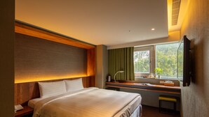 Habitación de hotel con una cama grande, un escritorio con silla, una ventana con cortinas y un televisor montado.