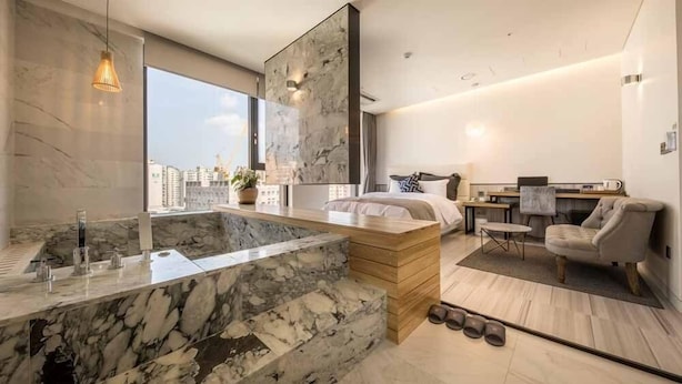 Ein modernes Hotelzimmer mit Marmorbad, einem großen Bett, einem Schreibtisch und Blick auf die Stadt.