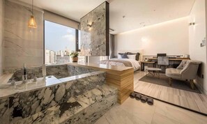 Une chambre d’hôtel moderne avec une salle de bain en marbre, un grand lit, un bureau et une vue sur la ville.