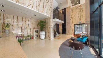 A modern lobby with marble walls, a reception desk, and a seating area with chairs.