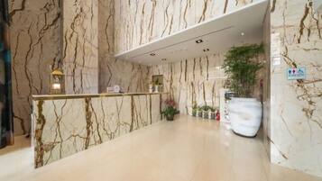 A marble reception area with a reception desk, potted plants, and a sign indicating accessibility.