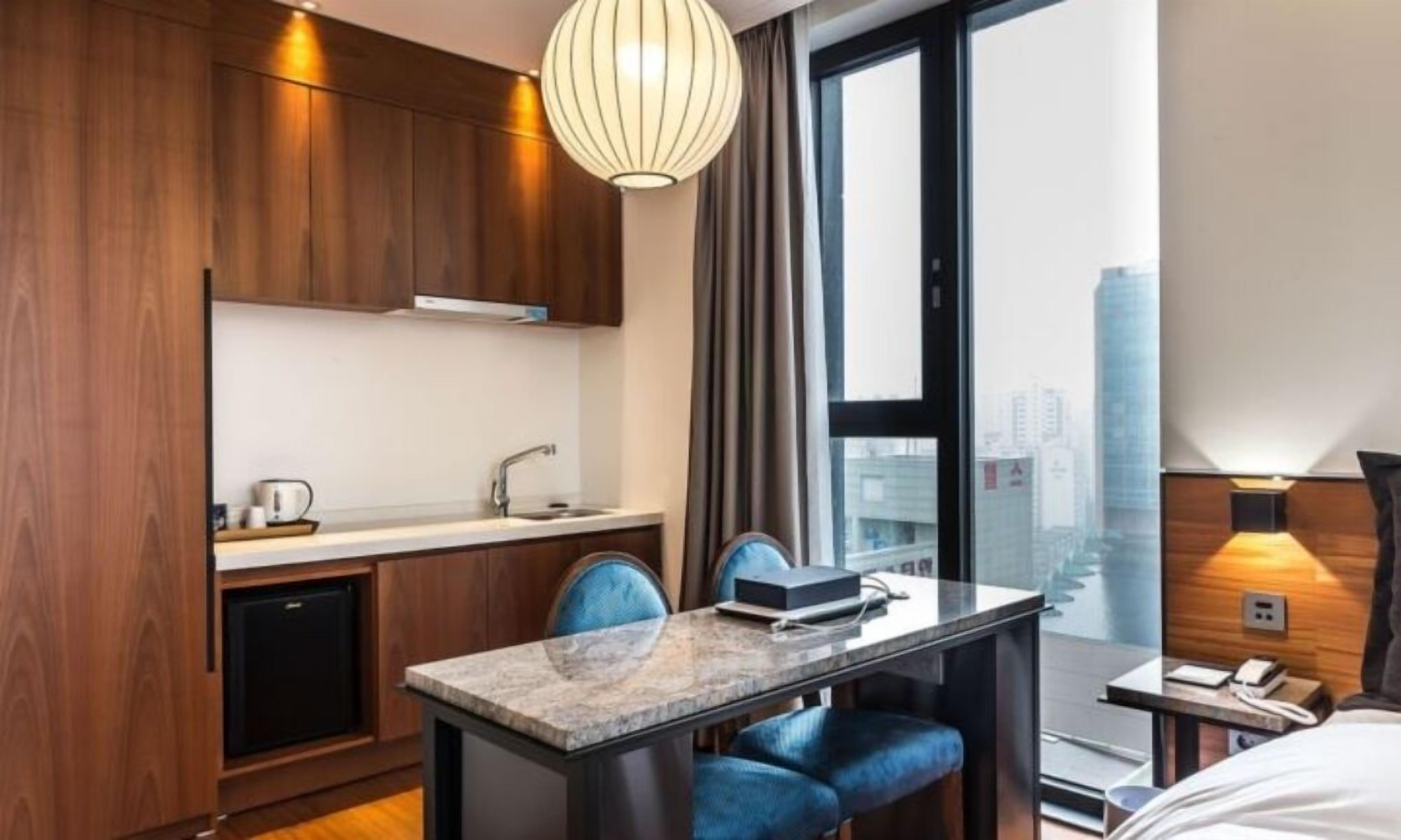 Quarto de hotel moderno com cozinha, mesa de jantar com cadeiras, cama e vista para a cidade.