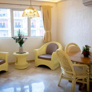 A room with wicker furniture, a dining table, a vase with flowers, and a window with curtains. - Clarkton Hotel (Angeles City)