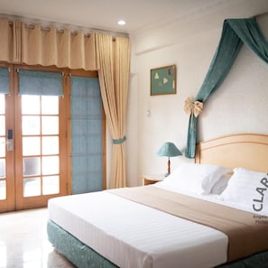 A hotel room with a bed, curtains, a nightstand, a lamp, and a wall decoration. - Clarkton Hotel (Angeles City)
