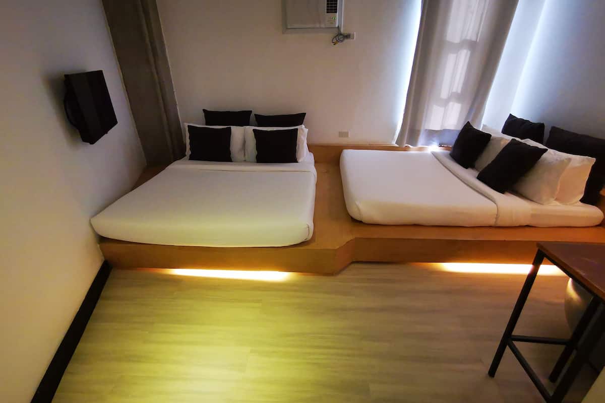 Une chambre d’hôtel moderne avec un lit sur une plateforme en bois, un lit plus petit et un bureau.