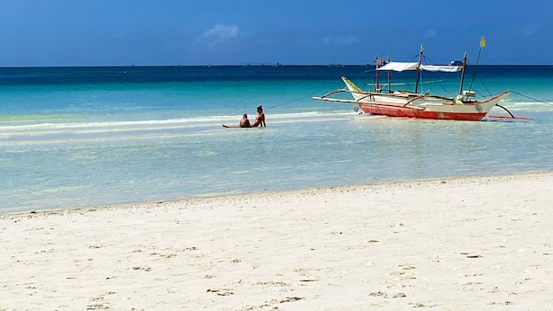 Une plage avec une eau turquoise et limpide, un bateau et une rive sablonneuse.