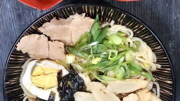 A plate of noodles with various toppings, including green onions and a boiled egg, alongside two small bowls containing kimchi and pineapple.