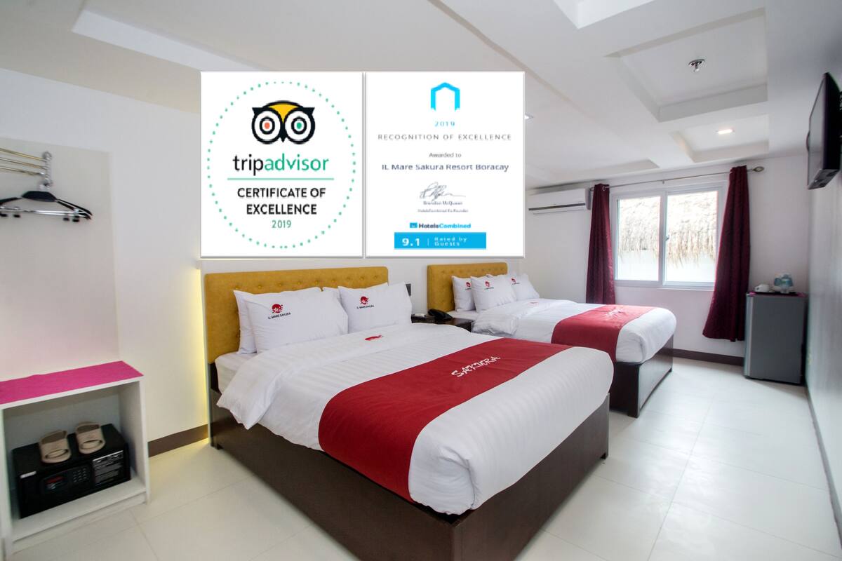 Habitación de hotel con dos camas, televisión, escritorio y ventana con cortinas. Hay diplomas en la pared.