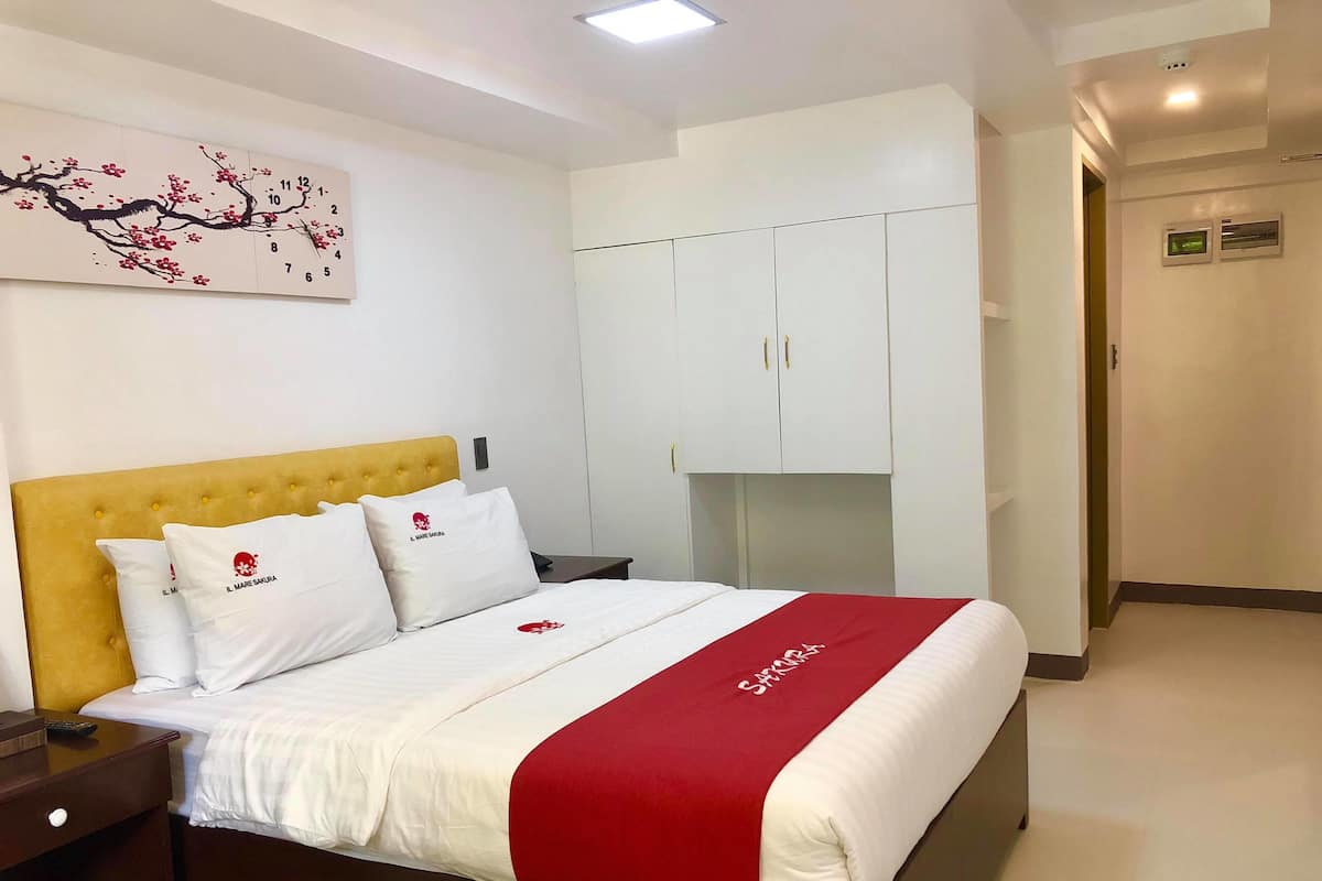 Una habitación de hotel con cama, mesita de noche, armario y una obra de arte colgada en la pared.