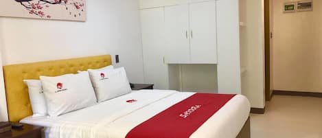 A hotel room with a bed, a nightstand, a wardrobe, and a wall-mounted artwork.