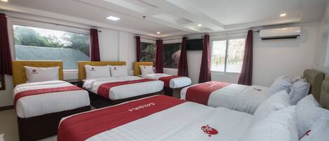 Une chambre d’hôtel avec quatre lits disposés en rangée, une grande fenêtre avec des rideaux et un appareil de climatisation fixé au mur.
