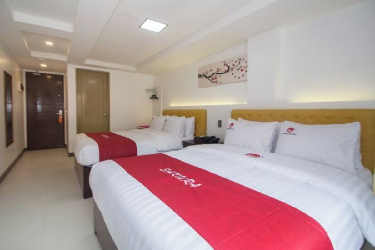 Habitación de hotel con dos camas, cada una con una colcha roja y blanca, un cabecero de madera y una obra de arte colgada en la pared.