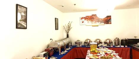 Una mesa de buffet con diversos alimentos y utensilios de servicio, una lámpara en el techo y obras de arte colgadas en la pared.