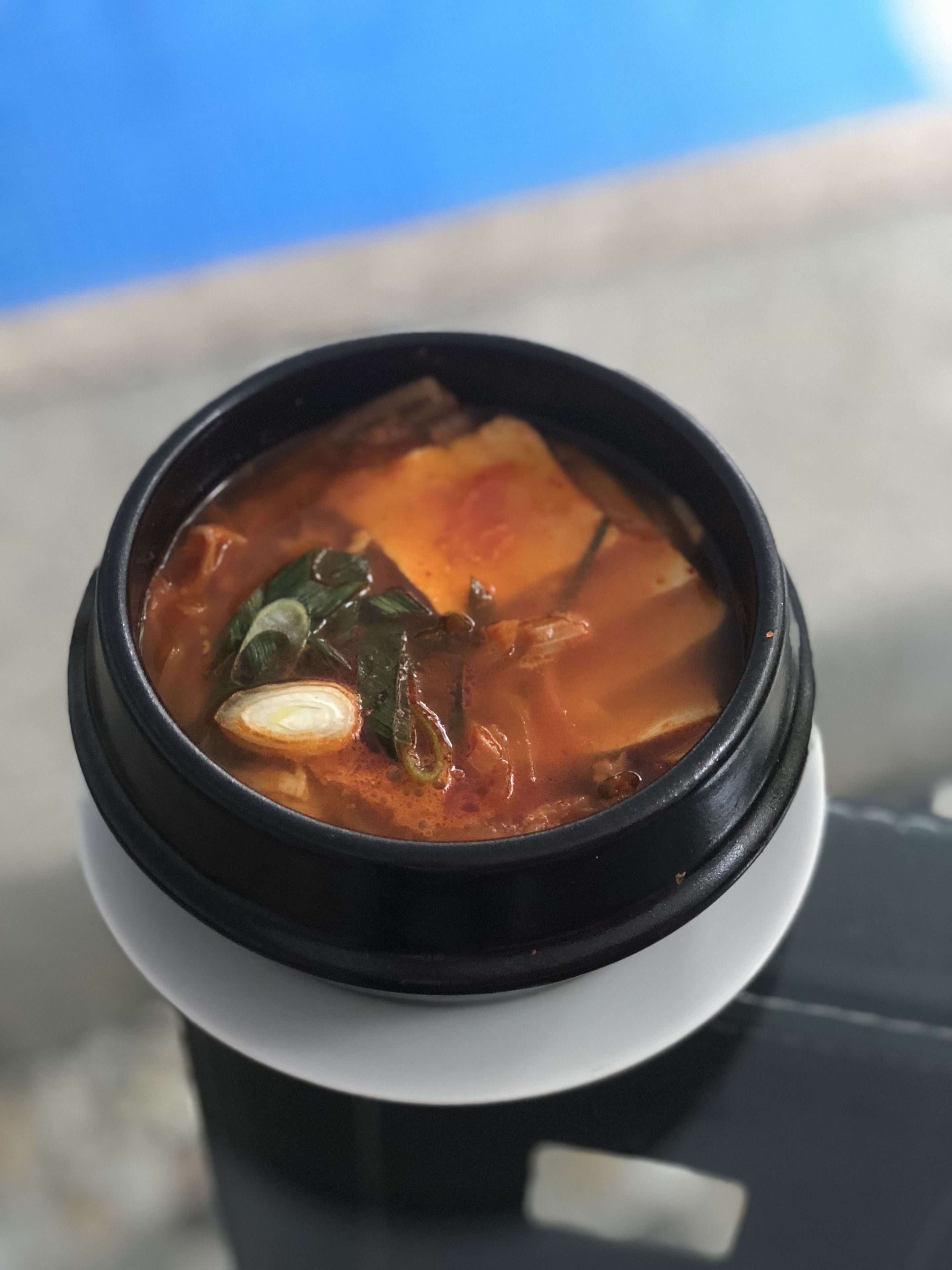 A cup of soup with a black lid and a white base, placed on a table.