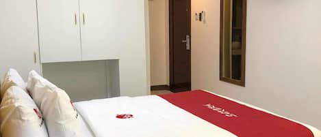 A hotel room with a bed, a TV mounted on the wall, a wardrobe, and a door leading to another room.