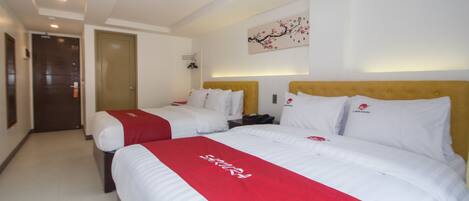 Habitación de hotel con dos camas, una toalla roja, un reloj en la pared y una puerta al fondo.