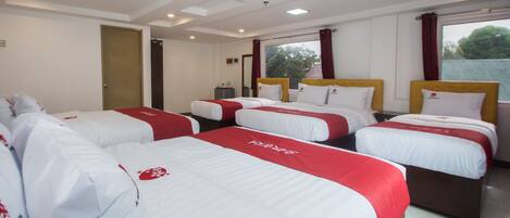 Habitación de hotel con cuatro camas dispuestas en fila, cada una con ropa blanca y detalles en rojo.