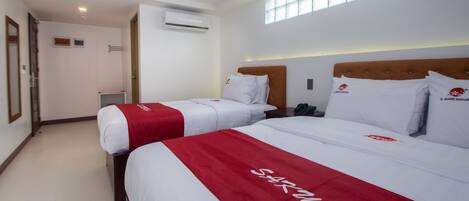A hotel room with two beds, each with a red and white bedspread, a wooden headboard, and a window providing natural light.