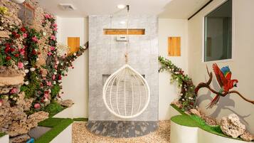 A modern bathroom with a stone wall, a hanging egg chair, and a parrot mural.