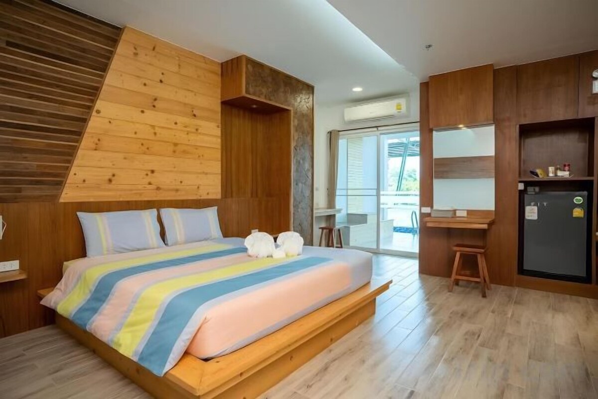 A bedroom with a bed, wooden headboard, a desk, and a refrigerator.
