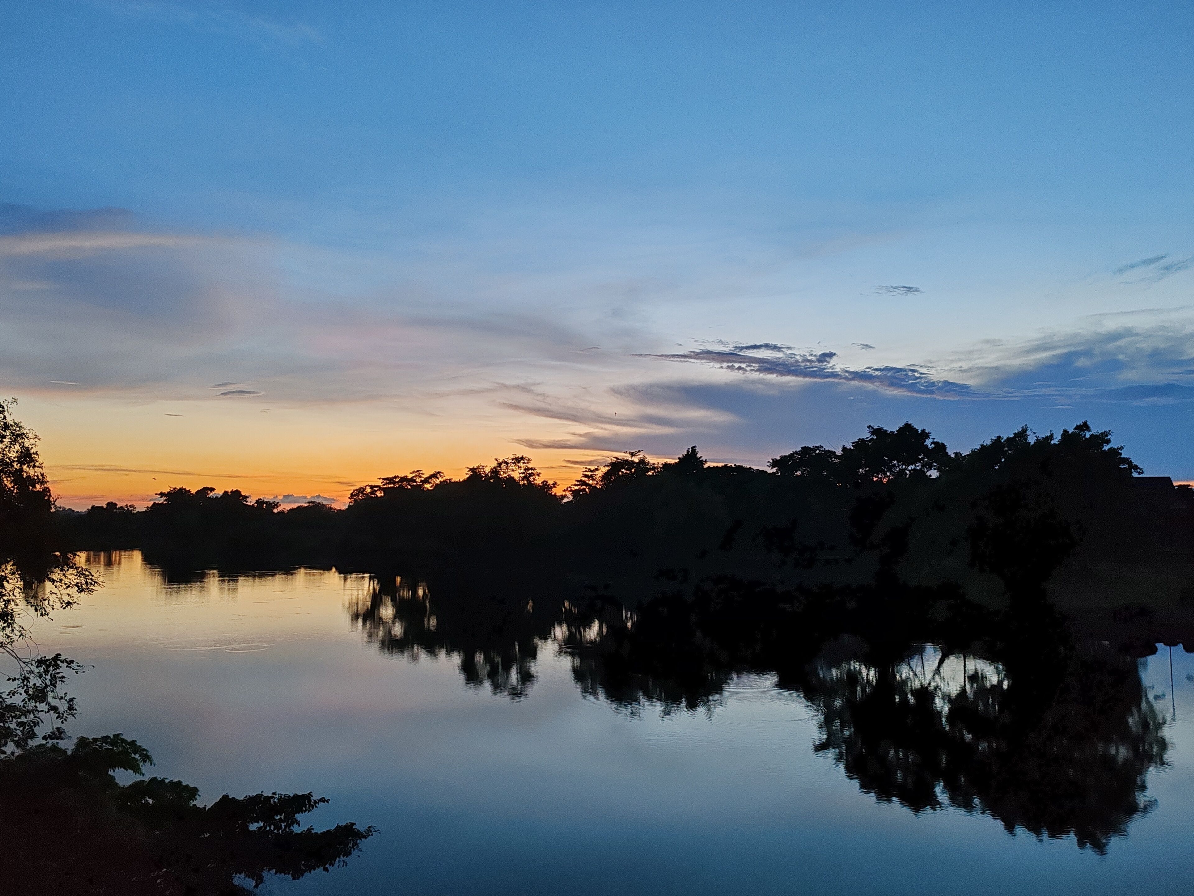 Un lago tranquilo al atardecer, con árboles reflejándose en el agua.
