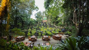 An outdoor restaurant with multiple wooden tables and chairs, surrounded by lush greenery and a waterfall. - Tamnanpar Resort and Water Park Rayong (Rayong)