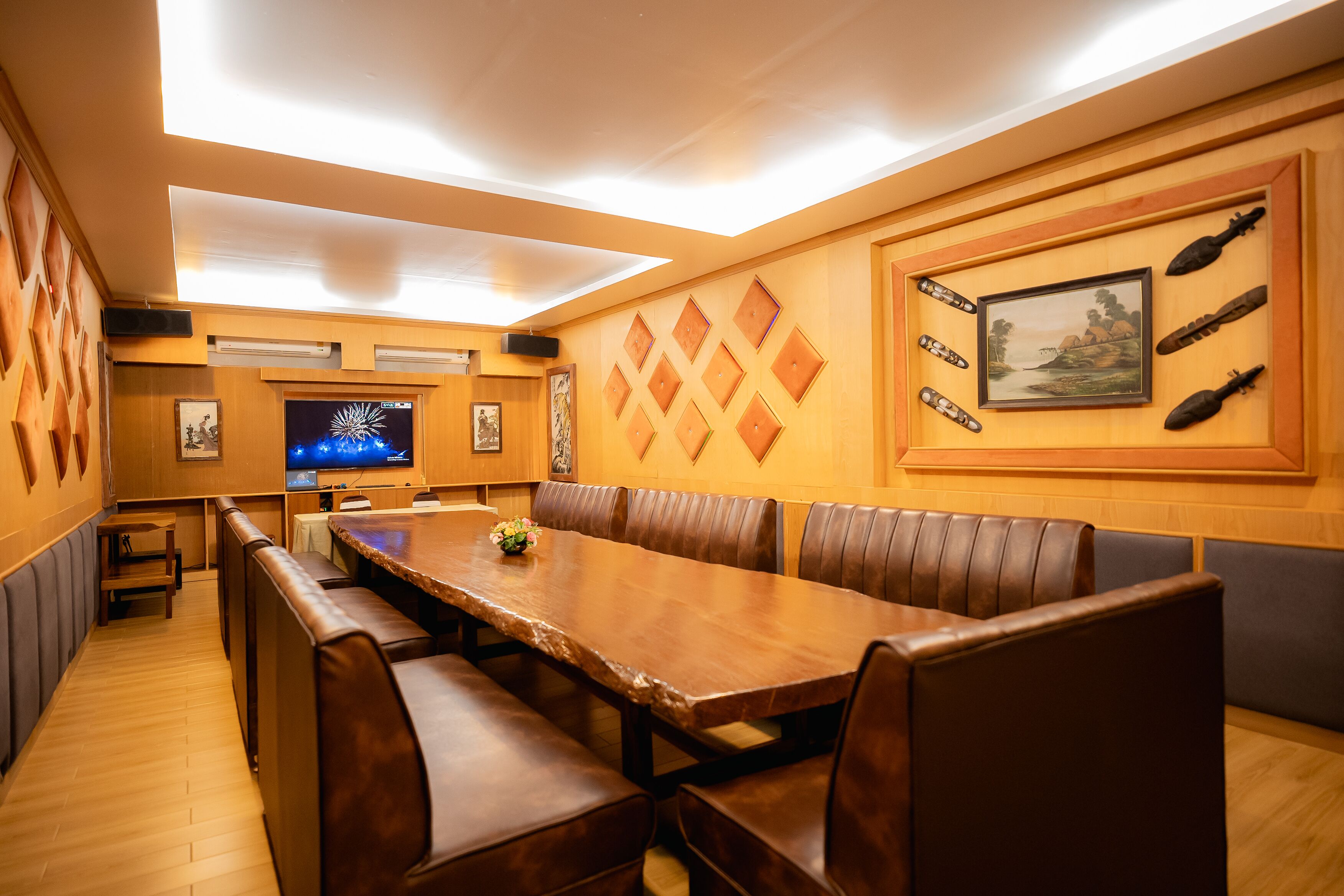 Un restaurante con una larga mesa de madera, cabinas acolchadas y un televisor montado en la pared.