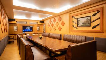 Un restaurante con una larga mesa de madera, cabinas acolchadas y un televisor montado en la pared.
