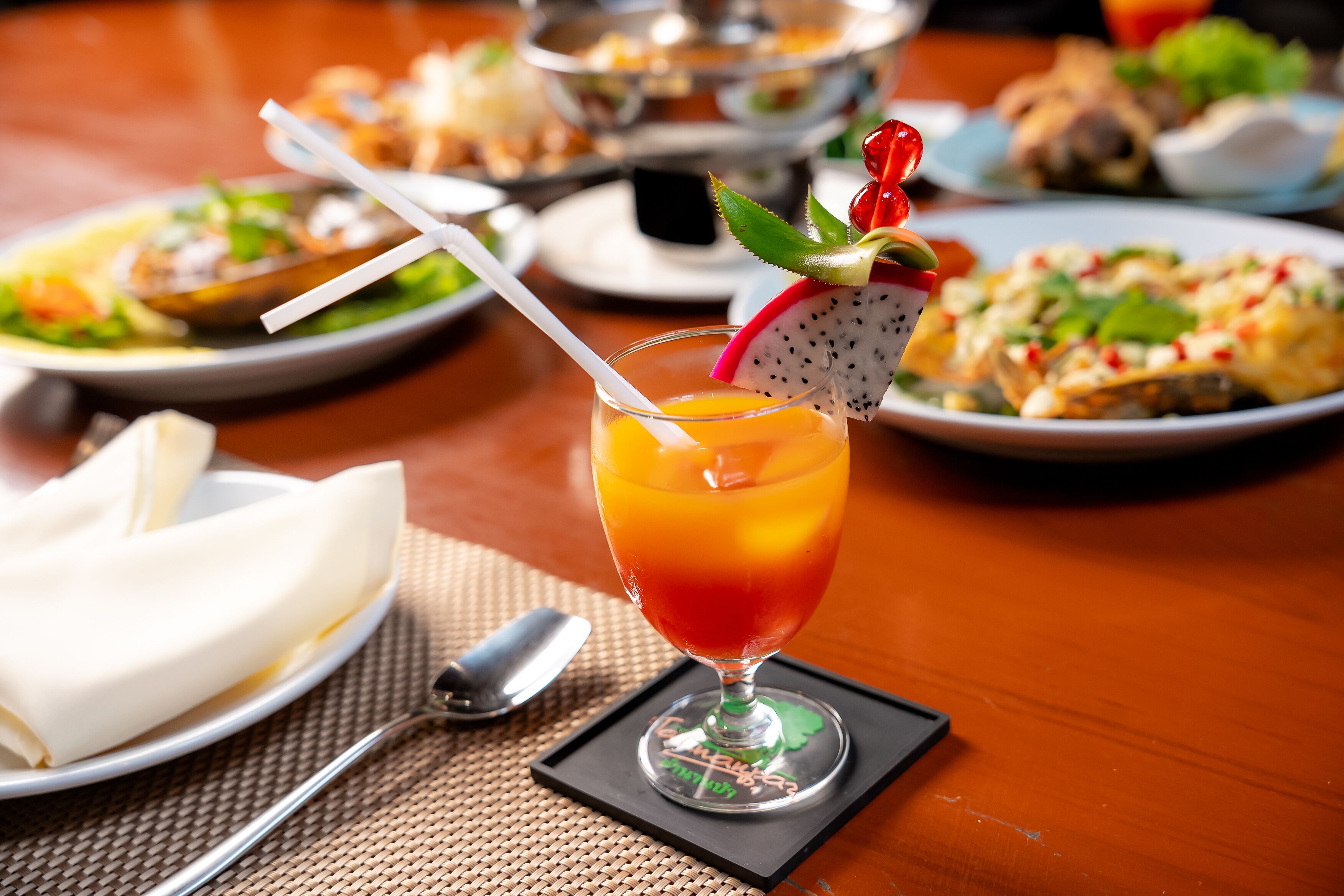 A table with various dishes, a glass of orange juice with a straw, and a napkin on a placemat.