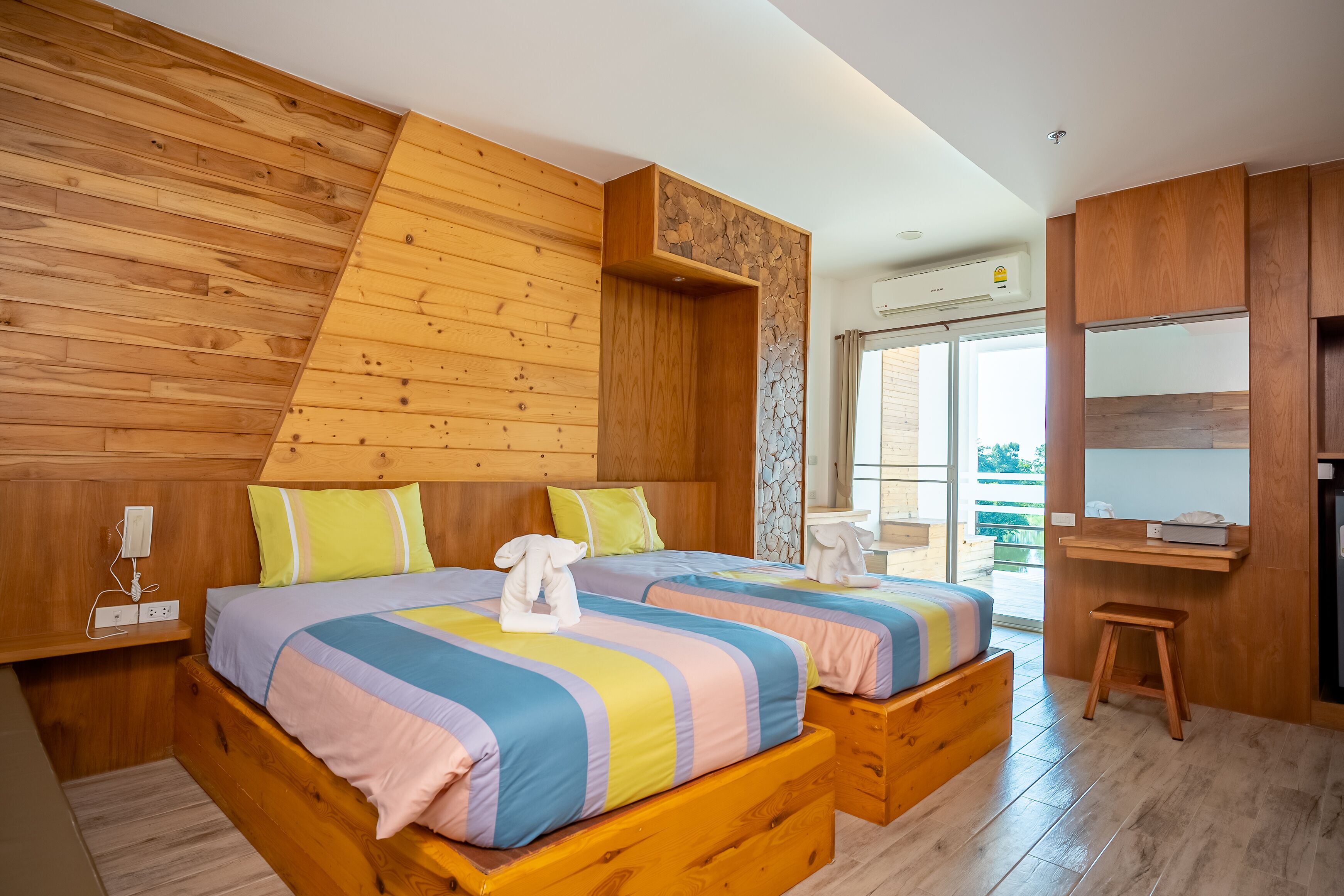 Ein modernes Schlafzimmer mit einem Holzkopfteil, einem großen Bett mit farbenfroher Bettwäsche, einem kleinen Hocker und einer eingebauten Ablagefläche.