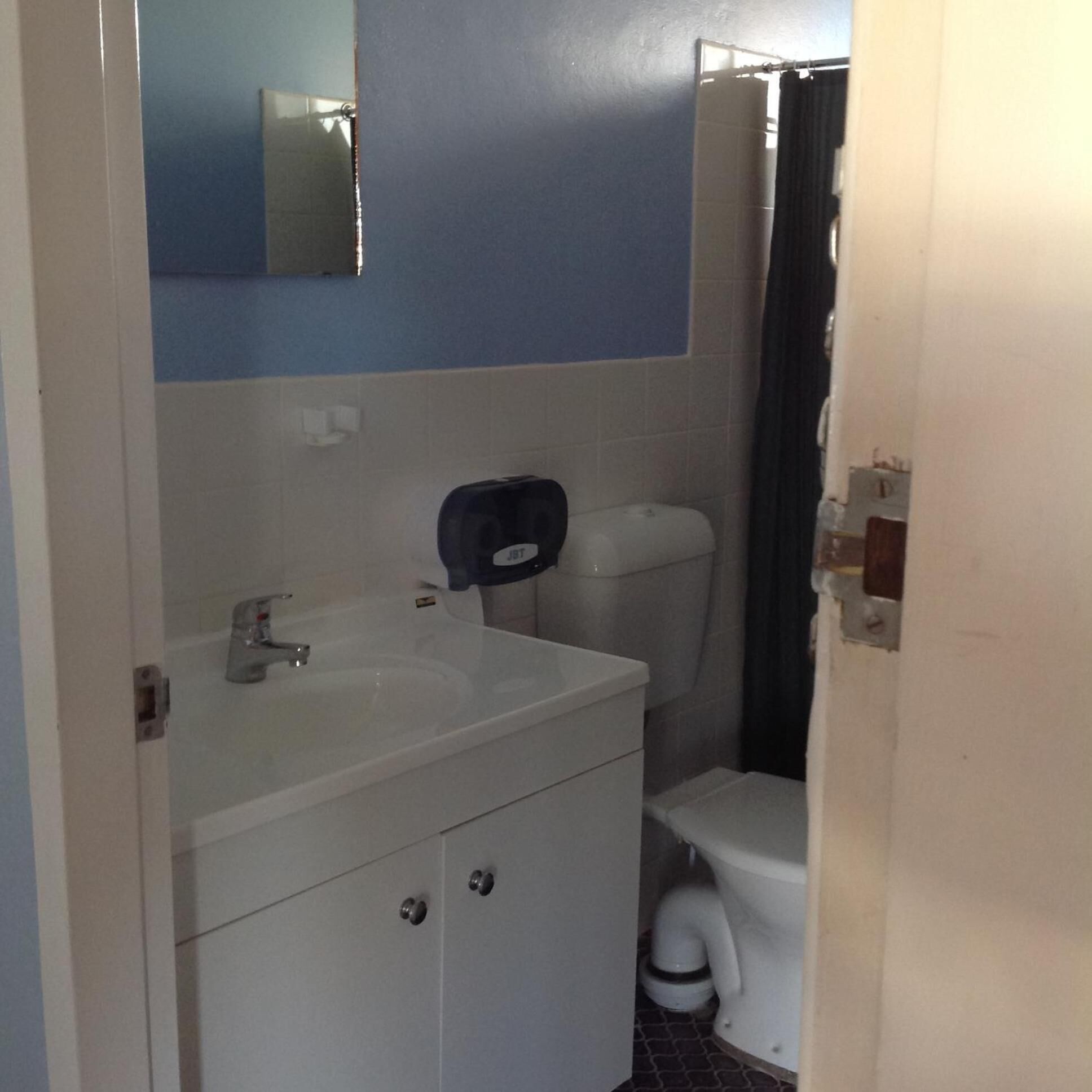 Un baño con un lavamanos blanco, un espejo encima, un inodoro y una cortina de ducha.