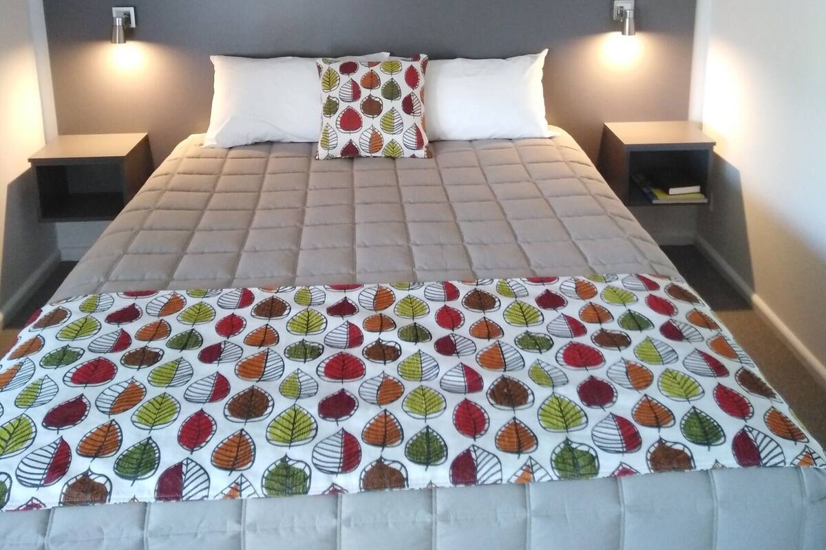 A neatly made bed with a patterned bedspread, two bedside tables with lamps, and a painting on the wall above the bed.