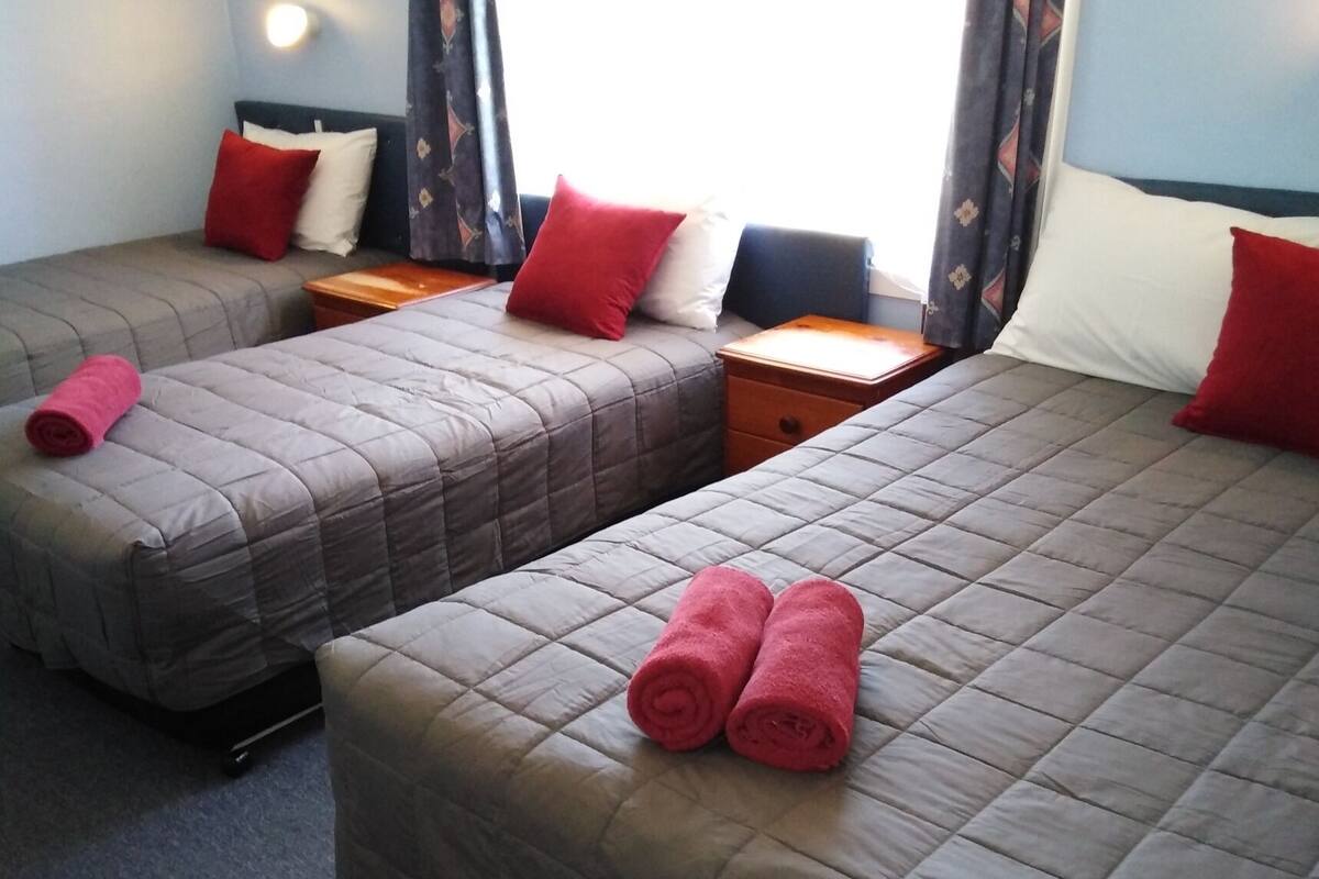A hotel room with two beds, each with a quilted bedspread and pillows, and a small table between them.