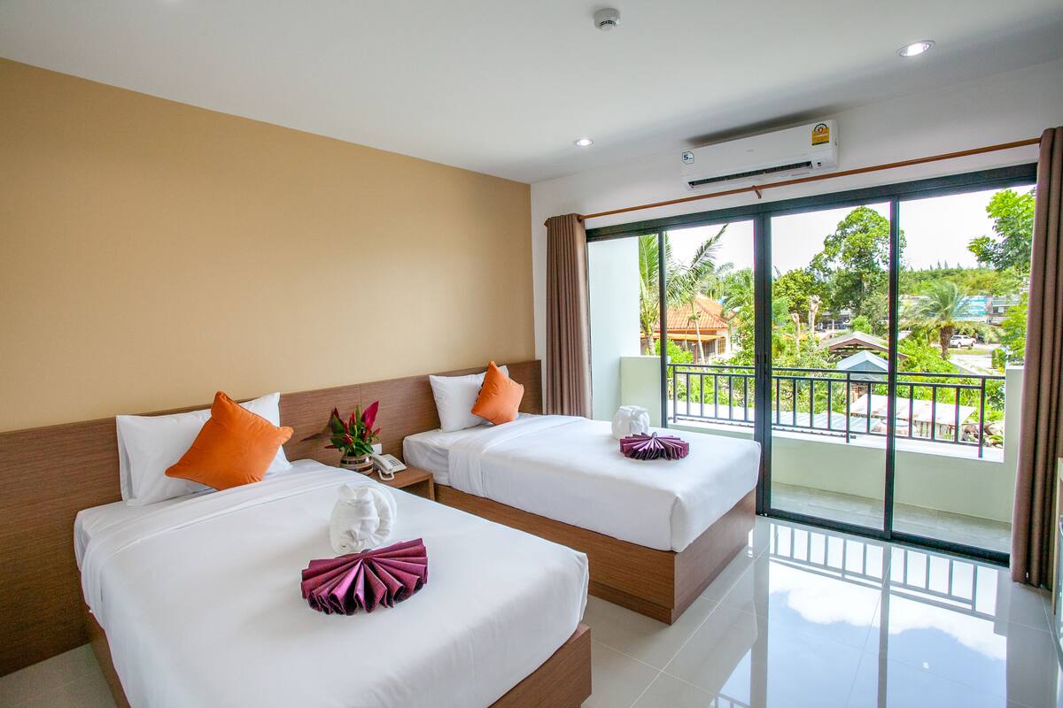 A hotel room with two beds, a balcony with a view of the outdoors, and an air conditioning unit on the wall.