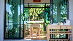 A modern interior with a wooden table and chairs, a glass door leading to an outdoor area with greenery. - Wanarom Residence Hotel (Krabi)