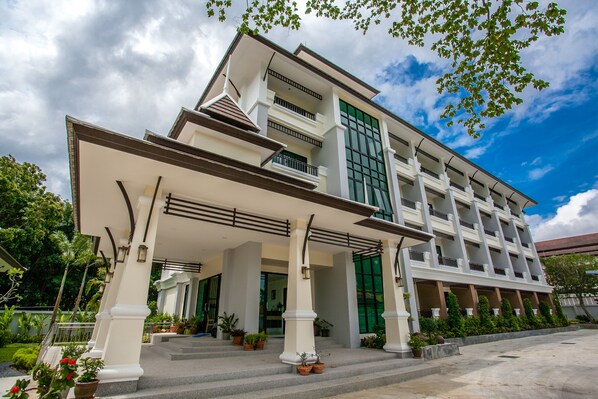 A multi-story hotel with a covered entrance, potted plants, and a clear sky. - Wanarom Residence Hotel (Krabi)