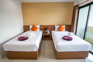Een hotelkamer met twee enkele bedden, houten hoofdborden, wit beddengoed, oranje kussens, een klein nachtkastje met een telefoon en een bloemenvaas.