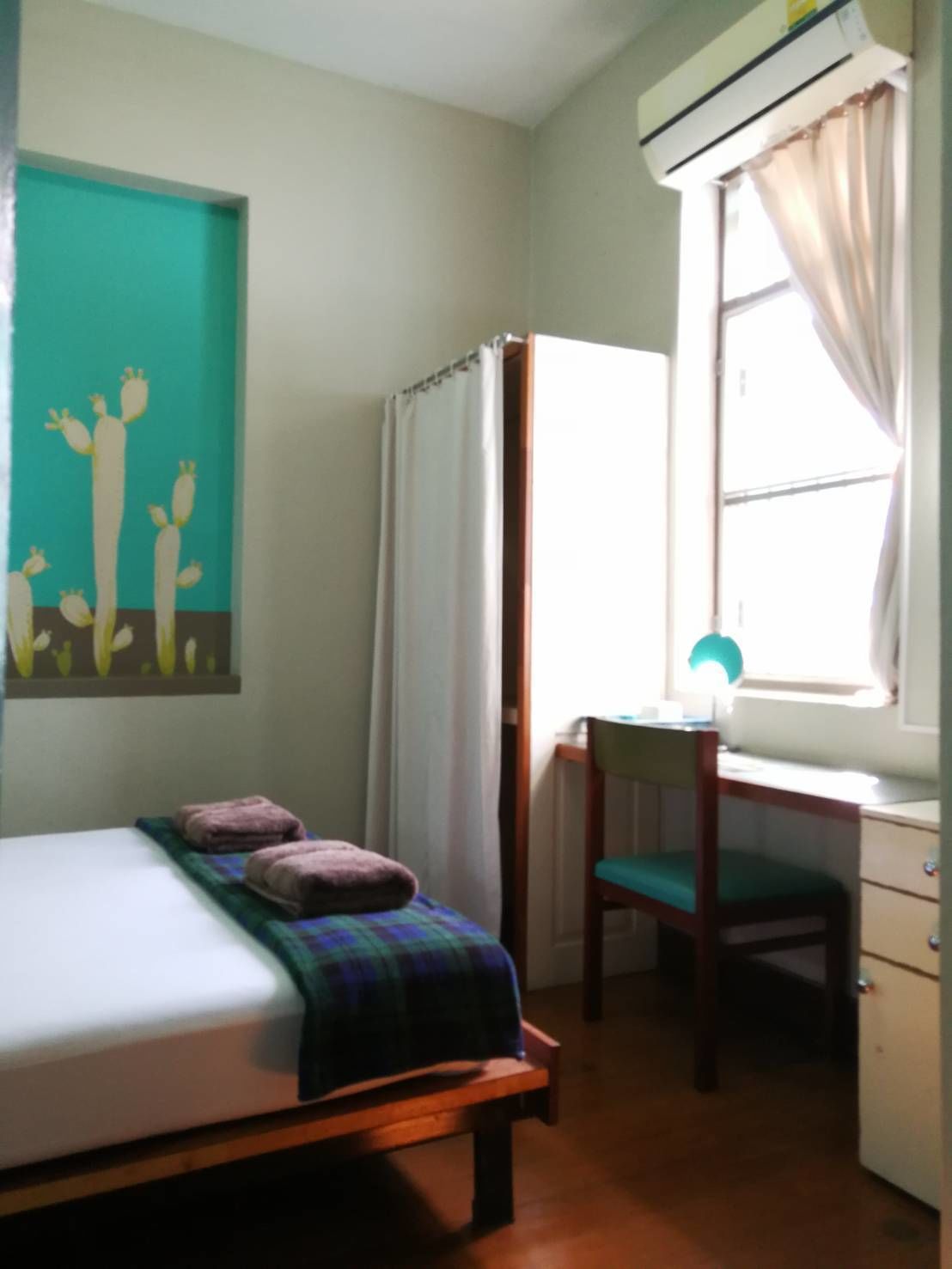 A bedroom with a bed, a desk, a chair, and an air conditioning unit.